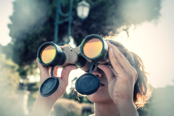 A girl looking around through a pair of military binoculars, finding something. White vignette. Nature setting.