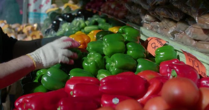 Grocery store employee puts peppers on food stand on city sidewalk.