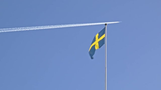 Swedish flag waving on the wind while plane flies in the background.