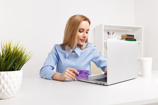 Office woman holding purple credit card and making shopping online at her workplace