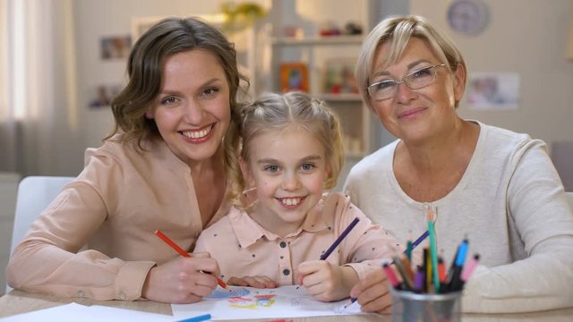 Happy child with mother and granny drawing pencils smiling on camera, family