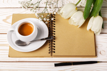 Woman working desk with coffee cup, paper notebook and white tulips. Mockup for greeting card. Flowers for mother's day