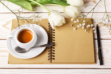 Woman working desk with coffee cup, paper notebook and white tulips. Mockup for greeting card. Flowers for mother's day