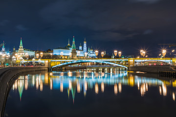 Fototapeta premium Illuminated Moscow Kremlin and Bolshoy Kamenny Bridge in the rays of setting sun. View from the Patriarshy pedestrian Bridge in Russia. Evening urban landscape in the blue hour