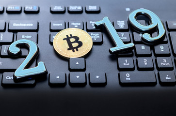 golden bitcoin It lies on the keyboard of a dark color. The inscription 2019. There is a toning