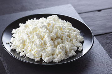 Cottage cheese on black slate board. Cheese on black plate. Soft cheese for diet on black boards. Healthy dairy product for breakfast. Concept