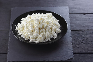 Cottage cheese on black slate board. Cheese on black plate. Soft cheese for diet on black boards. Healthy dairy product for breakfast. Concept