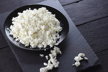 Cottage cheese on black slate board. Cheese on black plate. Soft cheese for diet on black boards. Healthy dairy product for breakfast. Concept