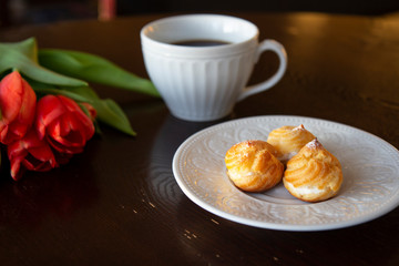 Close up of profiteroles dessert with bouquet of red tulips and a cup of black coffee in the background