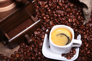 Fresh roasted coffee beans in burlap sack, espresso in cup and grinder on stone background.