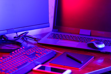 Workplace digital designer. Freelancer workplace in neon light. Computer, graphics tablet and smartphone on the table. Place for creativity in blue pink light