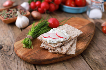 Fototapeta na wymiar crispbread with quark and fresh chive, radish and tomatoes on a rustic wooden table - healthy breakfast with fresh herbs 