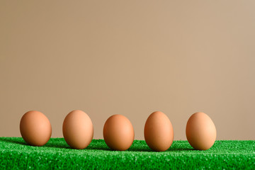 Eggs in a line lying on a green surface as a bottom frane, with a brown background. Easter concept.