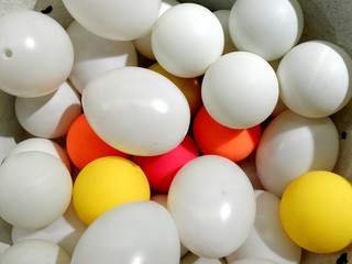 White plastic eggs and balls of different color laying together.