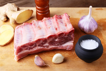 Raw ribs with a garlic, spices, ginger, salt and grinder on cutting board.
