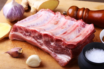 Raw ribs with a garlic, spices, ginger, salt and grinder on cutting board.
