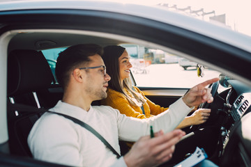 Driving school or test. Beautiful young pregnant woman learning how to drive car together with her...
