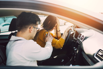 Driving school or test. Beautiful young pregnant woman learning how to drive car together with her instructor.