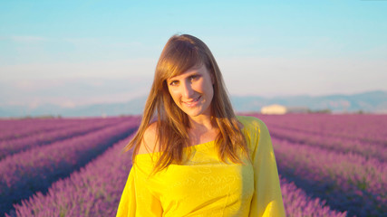 CLOSE UP: Smiling young woman walking through purple lavender field