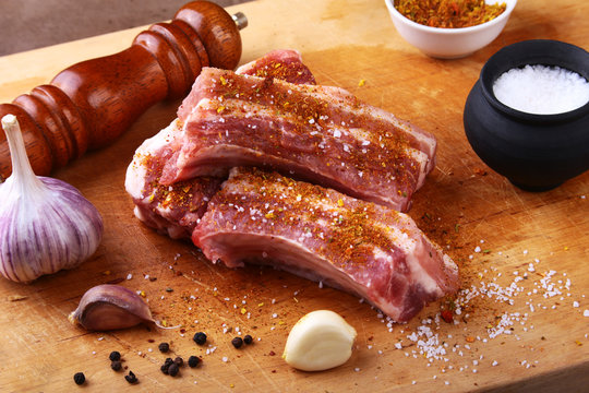 Raw ribs with a garlic, spices, ginger, salt and grinder on cutting board.