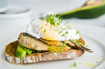 Sandwich with avocado, poached egg and sprats. White background, side view, close-up.