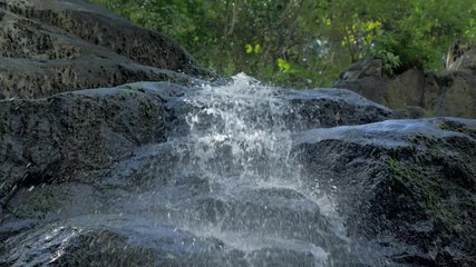 Close-up slow motion shot of small waterfall in the tropical rainforest jungle of Philippines. Small hidden rocky waterfall in jungle valley. Waterfall from a small mountain river in low mountains.