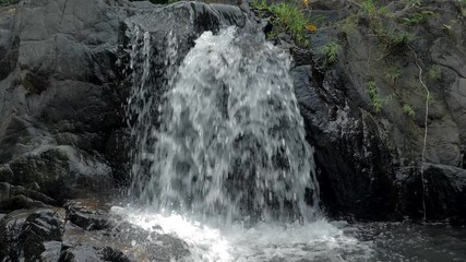 Close-up slow motion shot of small waterfall in the tropical rainforest jungle of Philippines. Small hidden rocky waterfall in jungle valley. Waterfall from a small mountain river in low mountains.