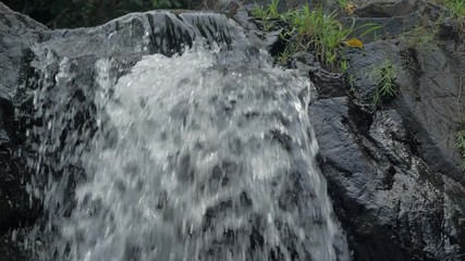 Close-up slow motion shot of small waterfall in the tropical rainforest jungle of Philippines. Small hidden rocky waterfall in jungle valley. Waterfall from a small mountain river in low mountains.