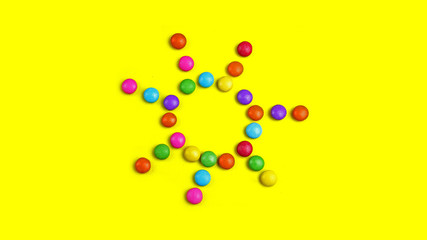 Colorful chocolade smarties on the yellow background . It is sun shape.