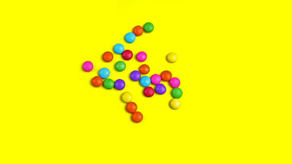 Colorful chocolade smarties on the yellow background.