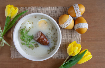 Wielkanocne śniadanie - żurek z jajkiemi i kiełbasą, obok pisanki, koszyczek ze świeconką