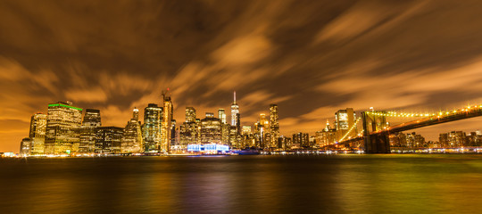 Fototapeta premium Manhattan panoramic skyline at night with Brooklyn Bridge. New York City, USA. Office buildings and skyscrapers at Lower Manhattan (Downtown Manhattan).