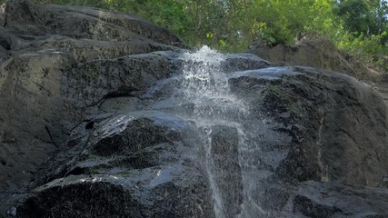 Close-up slow motion shot of small waterfall in the tropical rainforest jungle of Philippines. Small hidden rocky waterfall in jungle valley. Waterfall from a small mountain river in low mountains.
