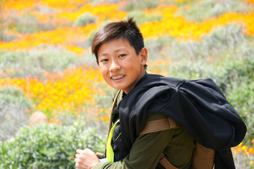 Young sporty Asian boy enjoying & hiking the mountain during the California Golden Poppy and Goldfields blooming in Walker Canyon, Lake Elsinore, CA. USA. Asian kid making his way through the mountain