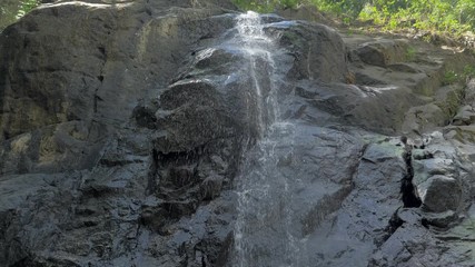 Close-up slow motion shot of small waterfall in the tropical rainforest jungle of Philippines. Small hidden rocky waterfall in jungle valley. Waterfall from a small mountain river in low mountains.