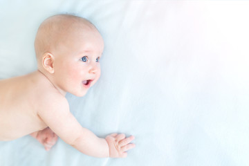Profile portrait of cute little baby boy lying on blue blanket and looking aside. Child with open mouth and wide opened eyes. Astonished surprised kid. Copyspace