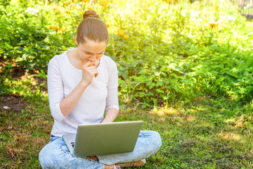 Freelance business concept. Young woman sitting on green grass lawn in city park working on laptop pc computer. Lifestyle authentic candid student girl studying outdoors. Mobile Office