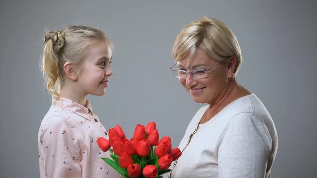 Beautiful senior lady taking flowers gift from granddaughter and hugging, love