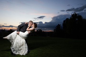 bride and groom dipping kiss in front of colorful sunset