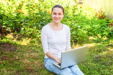 Freelance business concept. Young woman sitting on green grass lawn in city park working on laptop pc computer. Lifestyle authentic candid student girl studying outdoors. Mobile Office