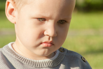 A little toddler boy is upset, sad, focused and serious. The child is offended. Portrait of a beautiful light-eyed boy close-up.