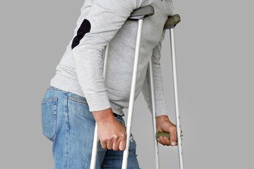 Man on crutches on a gray background. Close-up a elderly man walking with crutches.