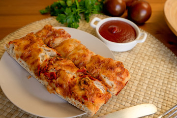 Oven-baked homemade focaccia bread with some ingredients on a plate, on a wooden kitchen table, view from the above
