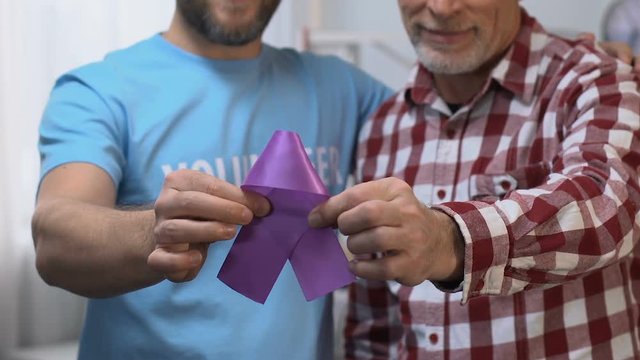 Two men holding violet ribbon, volunteer supporting old man, Alzheimers disease
