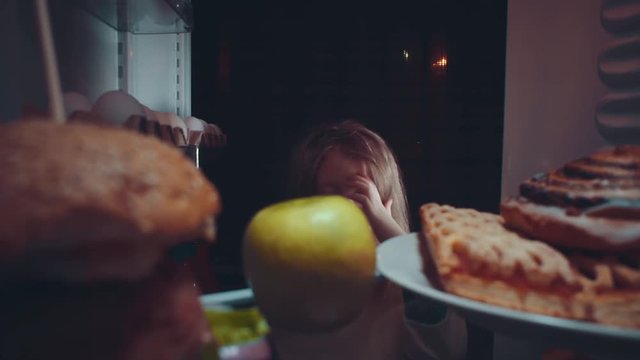 Little cute baby takes food out of the refrigerator at night, the problem of choosing between healthy and unhealthy food.Irregular nutrition and sleep disturbance.