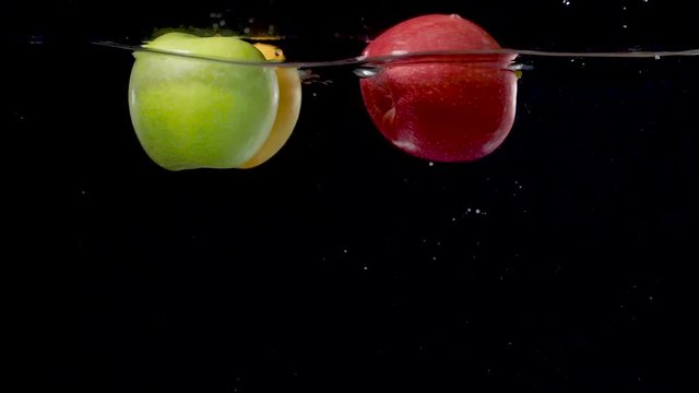 Beautiful yellow, green, and red apples floating in water in slow motion.