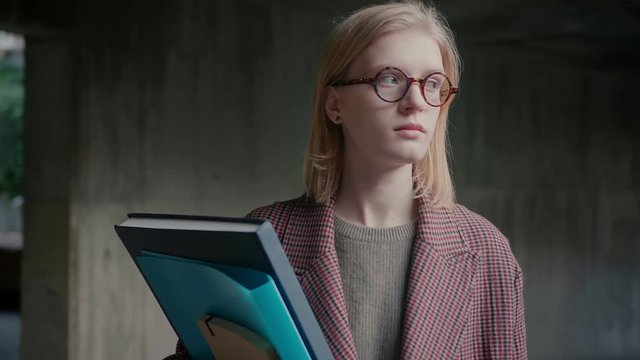 Close up of a student cute girl in brown coat with textbooks, waiting for classes, feeling outdoor intern campus feeling nervous anxious or on edge before exams