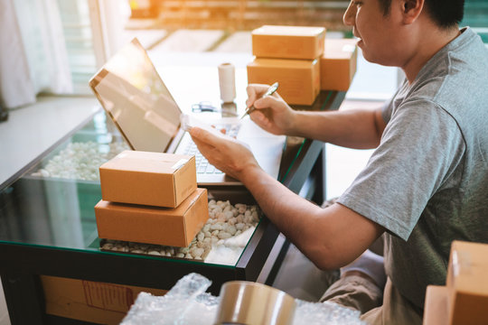 Young Asian Man Looking On Computer Laptop And Writing Order List On Paper, SME Concept.