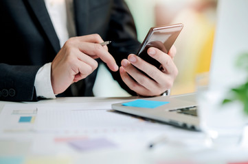 Shot of businessman working at office, holding pen and using smartphone. Business office working concept.