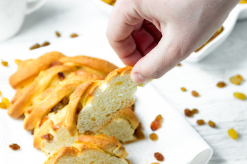 Hand holding Piece of Sweet Braided Bread with raisins on kitchen towel on white wooden background.